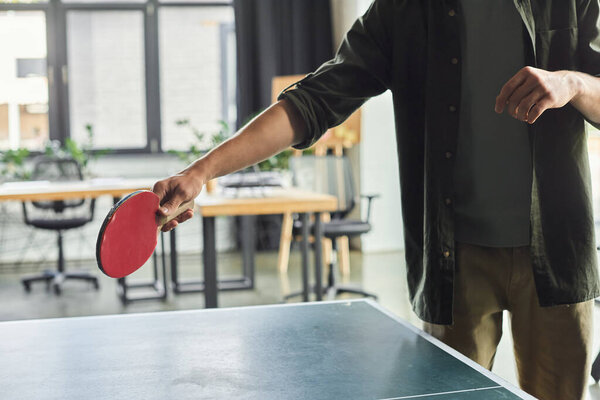 A person skillfully readies to hit a ping pong ball in a modern office with workstations.