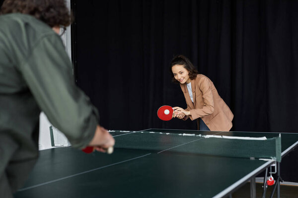 Two colleagues play ping pong in the office, boosting teamwork and camaraderie.