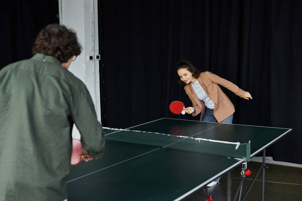 Two colleagues play ping pong, highlighting teamwork and relaxation during work hours.