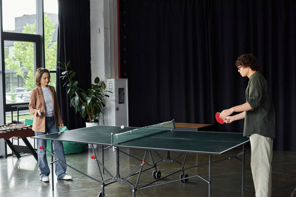 Two colleagues engage in a lively ping pong match during a break in their modern office space.
