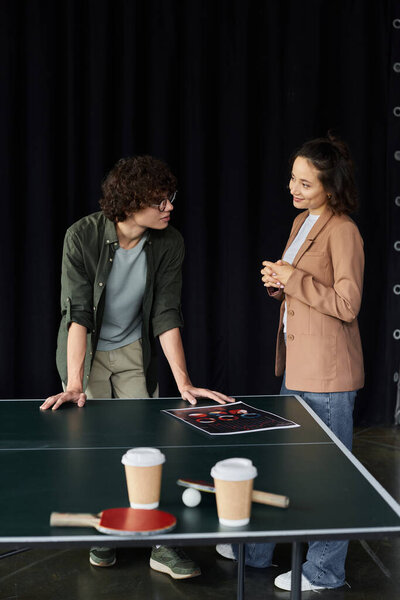 Two colleagues engage in a lively discussion over a table with work materials, cultivating ideas.