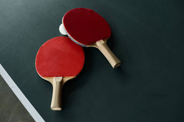 Two ping pong paddles rest beside a ball on a green table in a lively office environment.