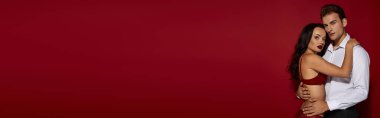 Bir çift, canlı kırmızı bir arka plana karşı hassas ve sevgi dolu bir anı paylaşıyor..
