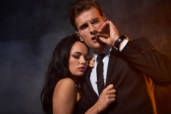 A loving couple stands close together, radiating passion in a mysterious, smoky setting.