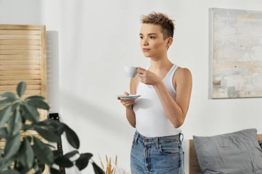 Güzel bir kadın, ışıkla dolu, modern, havadar bir odada kendine güvenen bir fincan çayla ayakta duruyor..