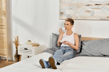 Genç bir kadın rahat bir şekilde yatağında oturur, vücuduna pozitif enerji saçarak zevkini çıkarır..