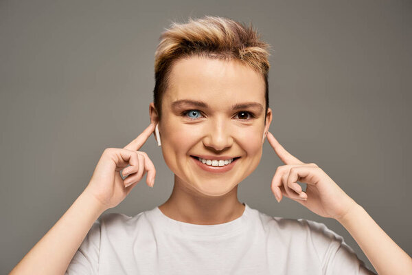 Молодая женщина с яркой улыбкой игриво закрывает уши, наслаждаясь любимыми мелодиями.