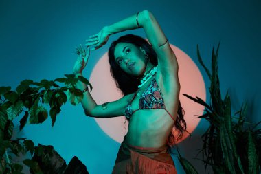 Güzel bir genç kadın yaz tarzını yemyeşil ve sanatsal aydınlatma arasında sergiliyor..