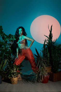 Parlak yaz kıyafetleri içindeki kendine güvenen genç kadın yemyeşil bitkiler ve ılık ışık arasında.