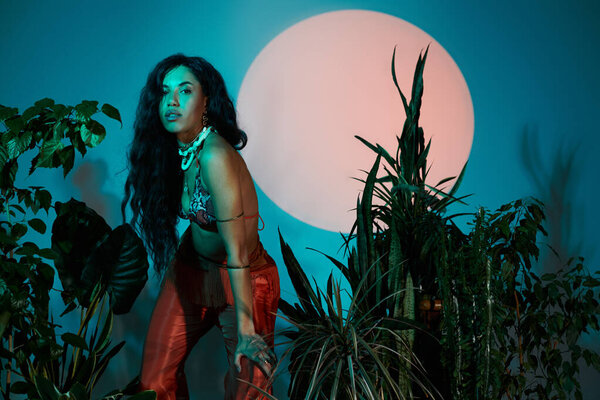 A beautiful young woman poses amidst lush greenery, exuding summer energy under soft lighting.