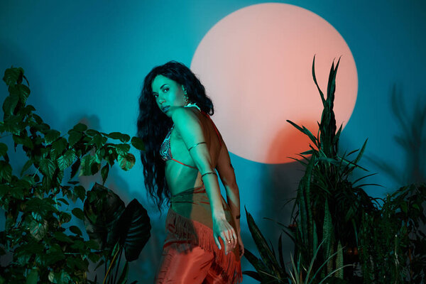 Woman in chic summer outfit poses gracefully in lush greenery at sunset.