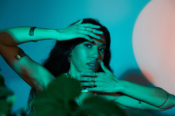 Graceful young woman poses amid lush plants and artistic shadows in summer style.