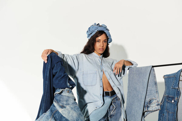 Striking young woman presents vibrant denim outfits with confidence in a sunlit studio.