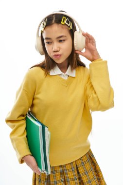 Şık okul üniformalı genç bir Asyalı kız kitaplarını tutarken rahat poz veriyor..