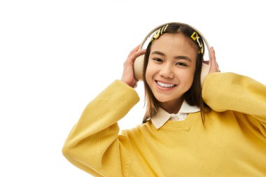 Şık üniformalı mutlu bir Asyalı kız parlak bir stüdyoda poz veriyor, müzikten hoşlanıyor..