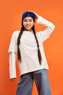 Neşeli bir Asyalı genç kız cesur bir turuncu arka plana karşı, modaya uygun bir şekilde poz veriyor..