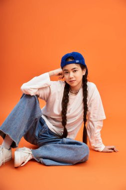 Modaya uygun bir genç kız, sıradan bir şekilde yerde oturuyor ve benzersiz tarzını bir stüdyoda sergiliyor..