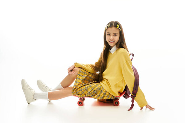 Молодая девушка в стильной форме улыбается, сидя на скейтборде.