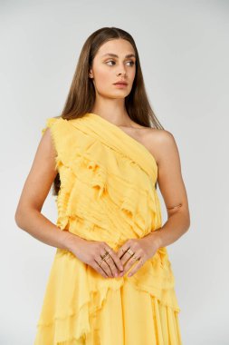 Büyüleyici kadın zarif bir şekilde duruyor, canlı sarı yaz kıyafetlerini duruşuyla sergiliyor..