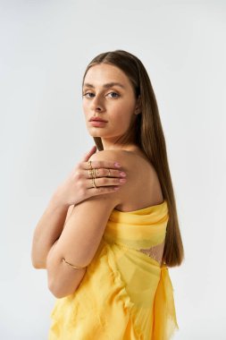 Genç bir kadın zarif tarzını ve doğal güzelliğini sergileyen açık sarı bir elbise giyer..