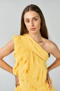 Göz kamaştırıcı genç bir kadın, parlak sarı bir elbise içinde, yaz havası ve tarzı yayarak rahatça poz veriyor..