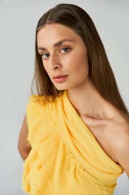 Genç bir kadın zarif bir şekilde parlak sarı bir elbiseyle poz veriyor, yaz aylarında kendine güveni yüksek..