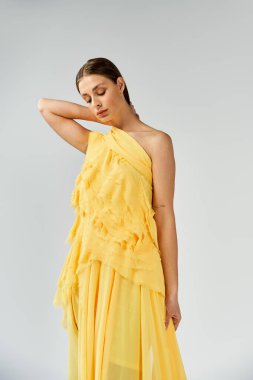 Güzel genç bir kadın zarif bir şekilde sarı elbiseyle poz veriyor..