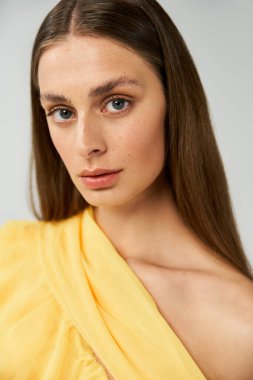 Genç bir kadın zarif bir şekilde poz veriyor. Parlak sarı bir elbise içinde, yaz stilini gösteriyor..