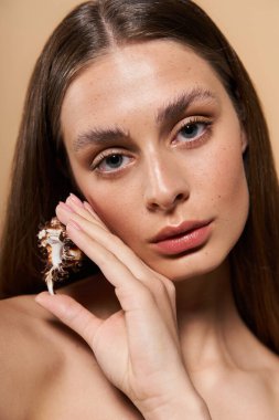 Genç bir kadın zarif bir şekilde yüzüne deniz kabuğu tutarak doğal güzelliğini ve yaz havasını sergiliyor..