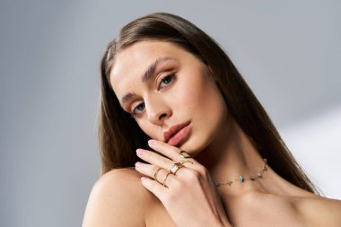 Uzun saçlı zarif genç bir kadın zarif bir poz veriyor, zarif mücevherlerini ve çekiciliğini ön plana çıkarıyor..