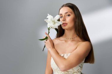 Genç bir kadın zarif bir şekilde beyaz bir çiçekle poz veriyor, şık yaz kıyafetleri ve güzellikleri sergiliyor..