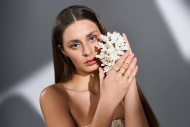 Genç bir kadın zarif bir şekilde yüzüne mercan tutarken güzellik ve tarz sergiliyor..