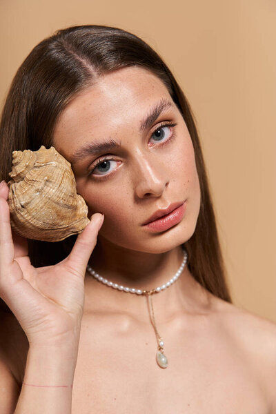 A young woman holds a seashell to her ear, capturing the essence of summer and natural beauty.