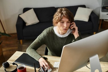 Genç bir öğrenci evde, telefonla konuşmak ve bilgisayar başında çalışmak arasında gidip geliyor..