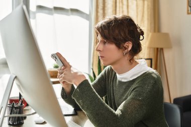 Genç bir öğrenci araştırma veya iletişim için akıllı telefonu kullanarak özenle evde çalışır..