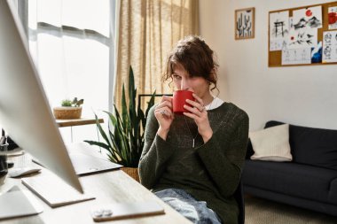 Genç bir adam çalışma masasında kırmızı bir kupayla rahatça oturup işine odaklanıyor..