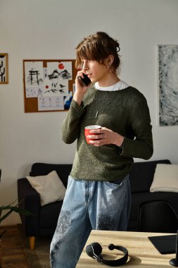 Genç bir öğrenci elinde fincanla evde duruyor, telefonla konuşuyor..