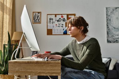 Genç bir adam parlak bir alanda bilgisayarla bir masada dikkatle çalışıyor..