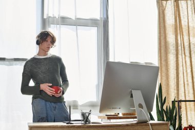 Bir öğrenci elinde fincanla masanın başında duruyor, güneşli bir odada derslerine odaklanıyor..