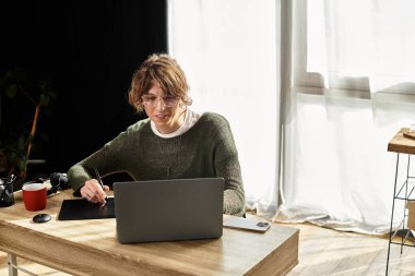 Öğrenci, iyi aydınlatılmış bir ev ortamında ahşap bir masada otururken dijital sanata odaklanıyor.