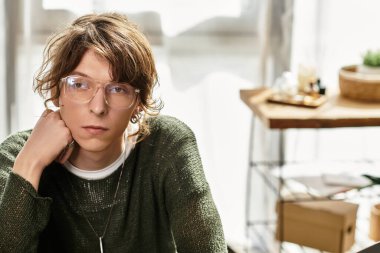 Gözlüklü genç bir adam rahat evinde otururken dalgın görünür..