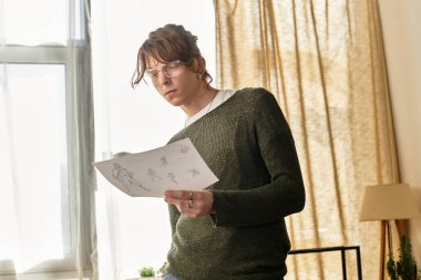 Genç adam, parlak bir öğleden sonra atmosferinde evde dinlenirken sanatsal çizimlerini gözden geçiriyor..