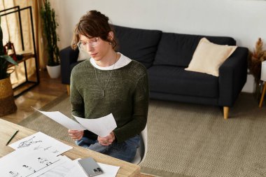 Sakin bir yerde, genç bir adam ilham kaynağıyla çevrili tasarımlarını inceliyor..