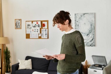 Odaklanmış genç adam notlarını kişisel sanat eserleriyle çevrili sıcak bir evde inceliyor..