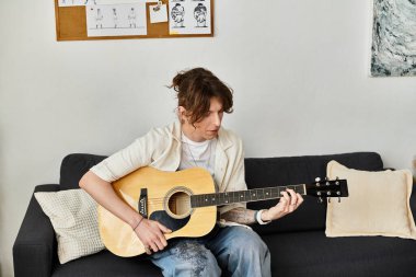 Genç bir adam evde gitar çalışıyor, rahat bir ortamda yeteneklerine odaklanıyor..