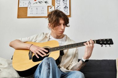 Genç adam kanepede oturur, gitar tıngırdatır düşünceli bir şekilde ev ortamında..