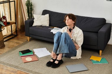 Etrafı dağınık kağıtlar ve aletlerle çevrili genç bir adam yerde oturuyor..