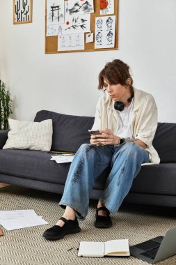 Öğrenci evde bir kanepede oturuyor. Etrafı kitap ve notlarla çevriliyken telefonuyla çok meşgul..