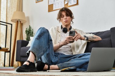 Evdeki adam rahat bir şekilde yerde oturuyor, çalışıyor ve akıllı telefonunu araştırma için kullanıyor..