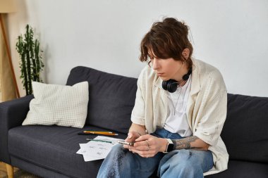 Genç adam öğrenme araçları ve notlarla çevriliyken evdeki mobil cihazına odaklanmış.